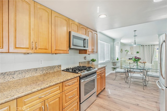 kitchen with light stone counters, stainless steel appliances, light brown cabinetry, light hardwood / wood-style flooring, and decorative light fixtures