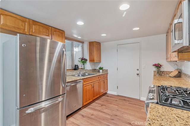 kitchen with light hardwood / wood-style flooring, appliances with stainless steel finishes, light stone countertops, and sink