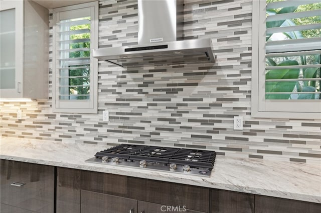 kitchen with dark brown cabinets, stainless steel gas stovetop, wall chimney range hood, and decorative backsplash