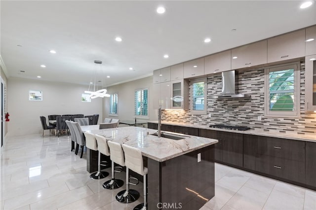 kitchen featuring a breakfast bar, backsplash, wall chimney exhaust hood, ornamental molding, and sink