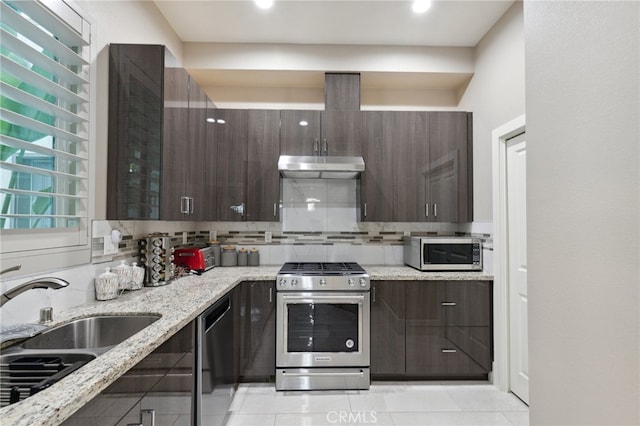 kitchen with appliances with stainless steel finishes, decorative backsplash, light stone counters, dark brown cabinetry, and sink