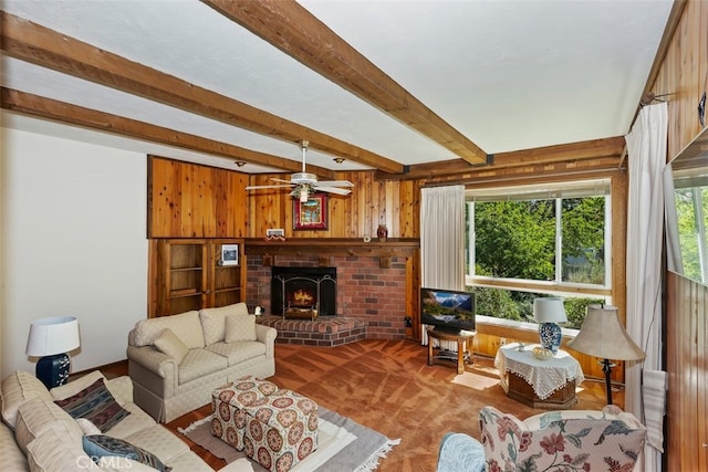 carpeted living room featuring ceiling fan, beam ceiling, a fireplace, and wooden walls