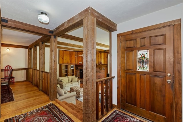 entryway featuring beam ceiling, wood walls, light hardwood / wood-style flooring, and a textured ceiling