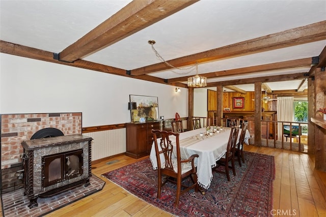 dining space featuring wooden walls, beamed ceiling, hardwood / wood-style floors, a chandelier, and a wood stove