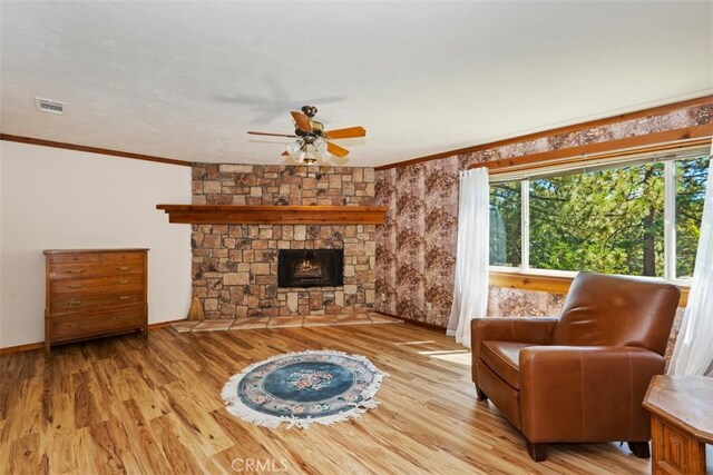 living room with a fireplace, light hardwood / wood-style floors, ceiling fan, and crown molding