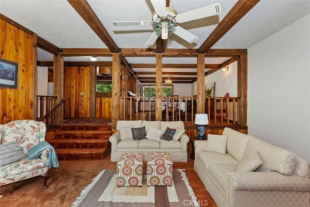 living room with ceiling fan, stairway, beamed ceiling, and wood walls