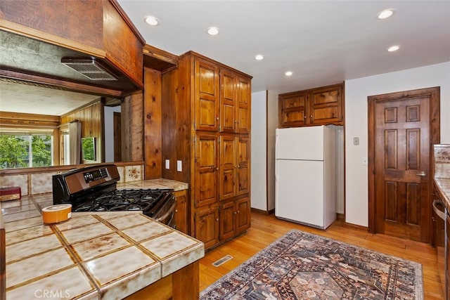 kitchen with tile countertops, white fridge, black range with gas stovetop, and light hardwood / wood-style flooring