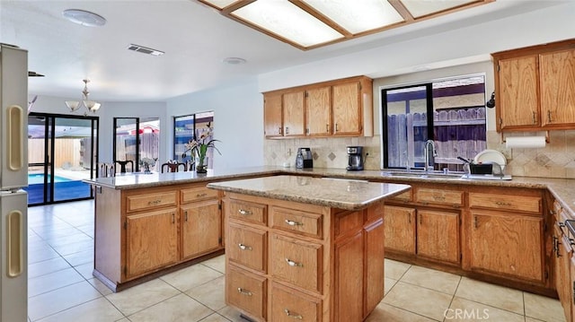 kitchen with an inviting chandelier, decorative backsplash, a center island, refrigerator, and sink