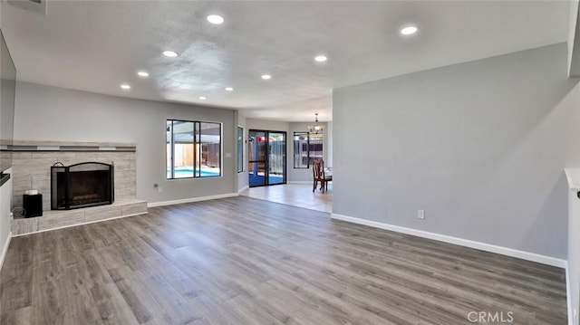 unfurnished living room featuring a tiled fireplace, an inviting chandelier, and wood-type flooring