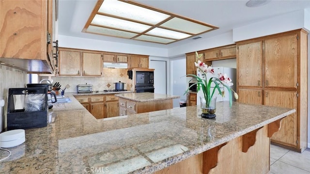 kitchen featuring decorative backsplash, kitchen peninsula, light stone countertops, and black appliances