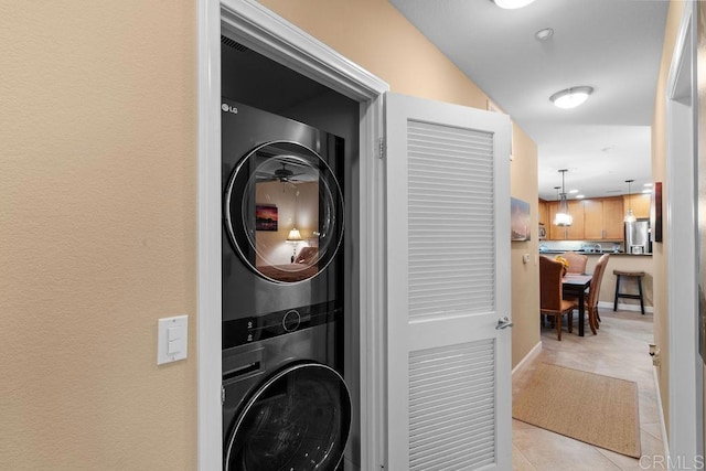 washroom featuring light tile patterned flooring, laundry area, baseboards, and stacked washer and dryer