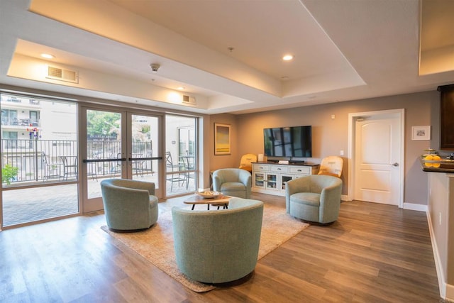 living area with a tray ceiling, visible vents, wood finished floors, and french doors