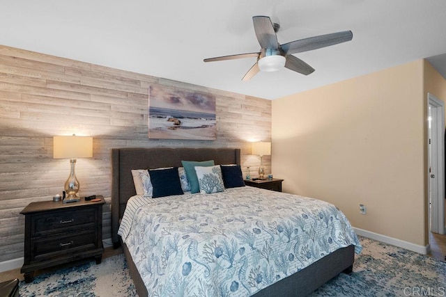 bedroom featuring an accent wall, wooden walls, baseboards, and ceiling fan