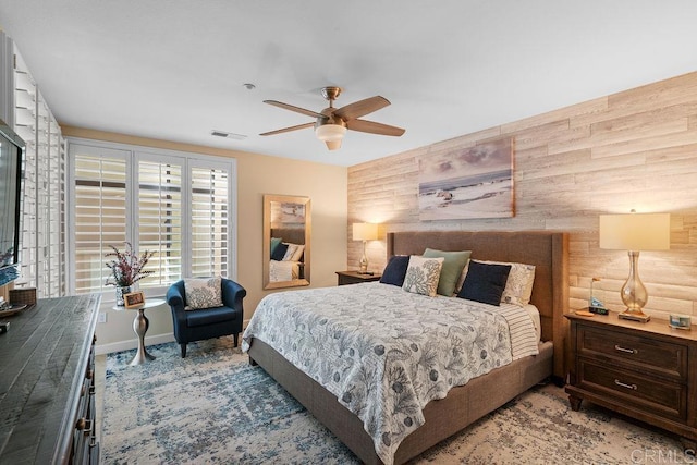 bedroom featuring visible vents, baseboards, wood walls, and a ceiling fan