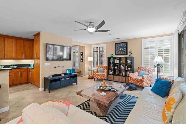 living room with light tile patterned floors, visible vents, baseboards, and a ceiling fan