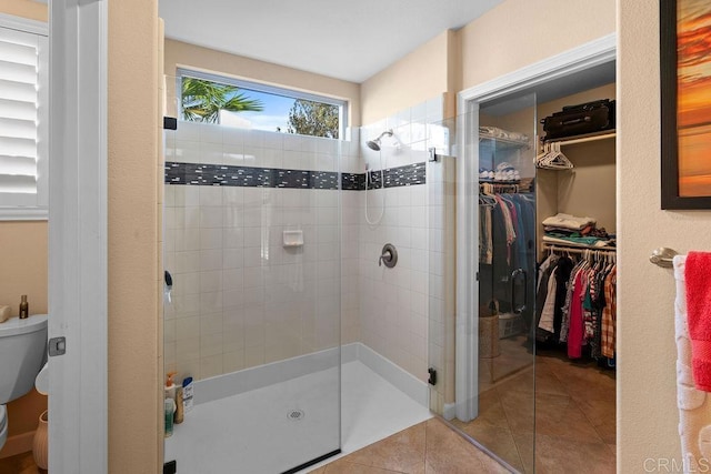 bathroom with tile patterned flooring, a walk in closet, toilet, and a stall shower