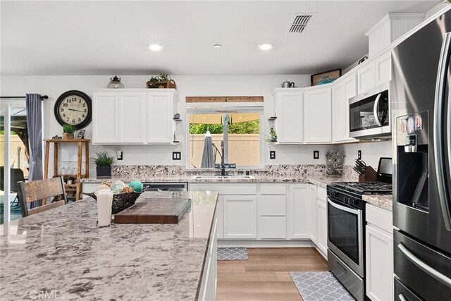 kitchen with light stone counters, appliances with stainless steel finishes, white cabinetry, light hardwood / wood-style flooring, and sink