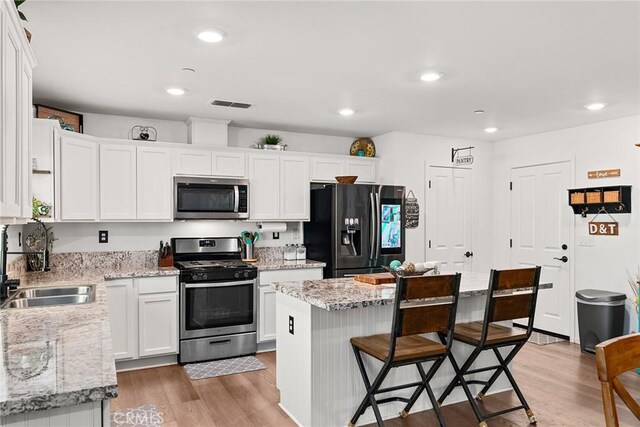 kitchen featuring white cabinetry, light hardwood / wood-style flooring, stainless steel appliances, sink, and a center island