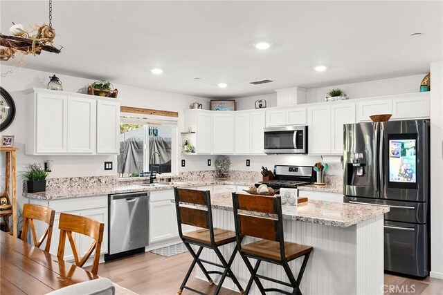 kitchen with stainless steel appliances, light stone countertops, a center island, light wood-type flooring, and white cabinetry