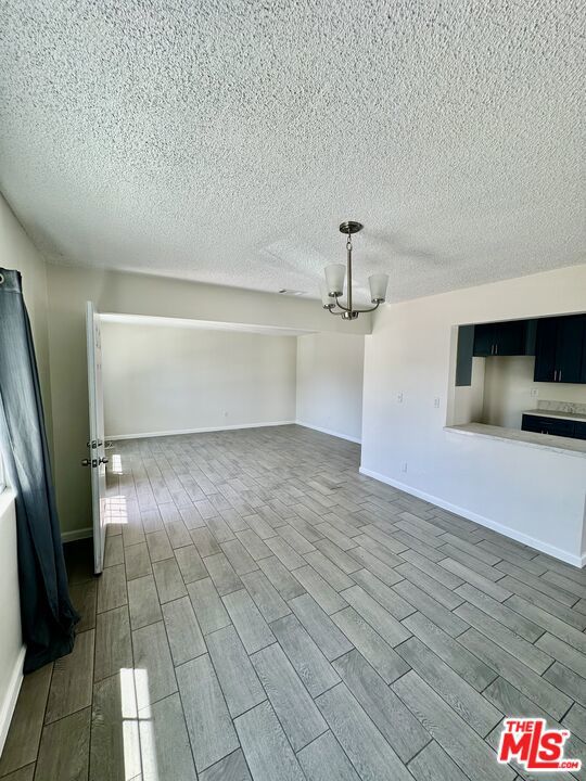 unfurnished living room featuring a chandelier, a textured ceiling, and hardwood / wood-style flooring