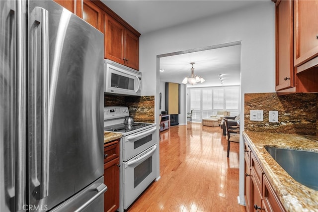 kitchen with light wood-type flooring, a chandelier, white appliances, decorative light fixtures, and light stone countertops