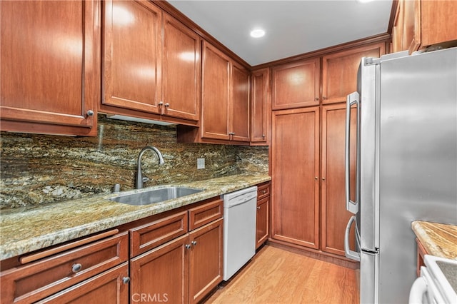 kitchen with white dishwasher, sink, tasteful backsplash, stainless steel refrigerator, and light wood-type flooring