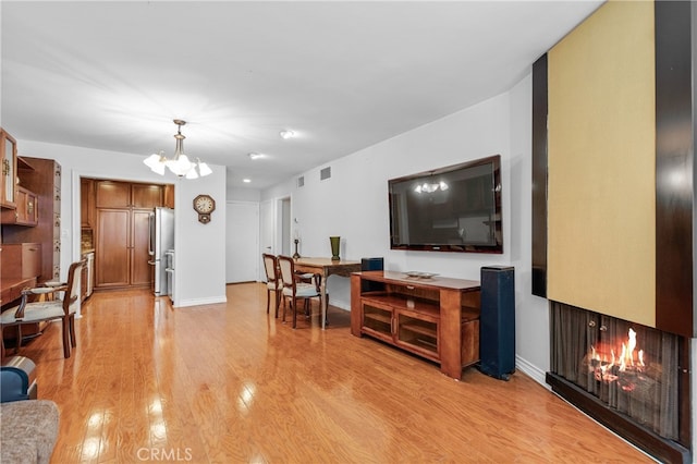 living room featuring light hardwood / wood-style flooring, a multi sided fireplace, and a chandelier