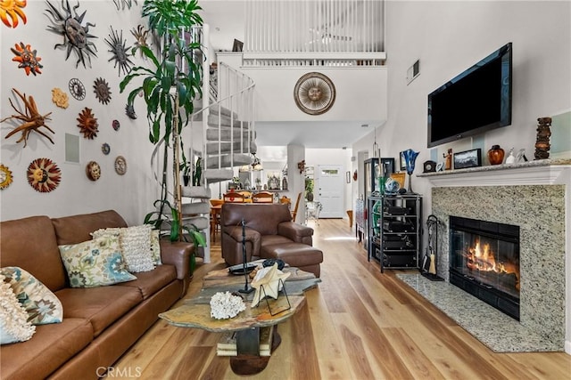 living room featuring wood-type flooring, a towering ceiling, and a premium fireplace