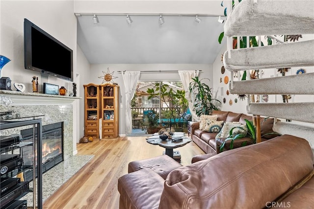 living room with a high end fireplace, light hardwood / wood-style floors, track lighting, and lofted ceiling