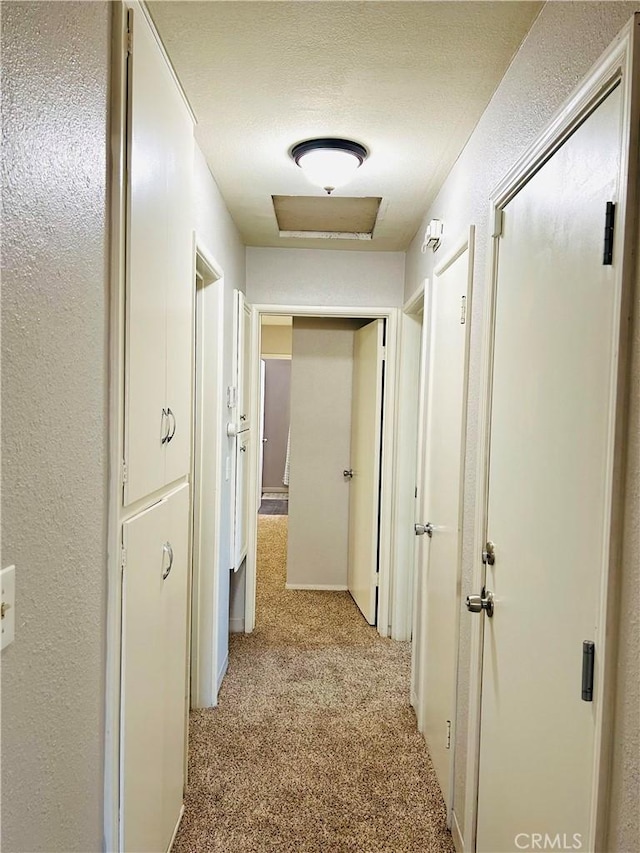 corridor with light colored carpet and a textured ceiling