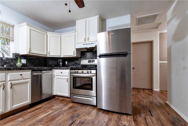 kitchen featuring under cabinet range hood, stainless steel appliances, decorative backsplash, and white cabinetry