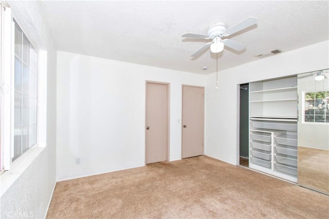 unfurnished bedroom featuring a textured ceiling, carpet, two closets, a ceiling fan, and visible vents