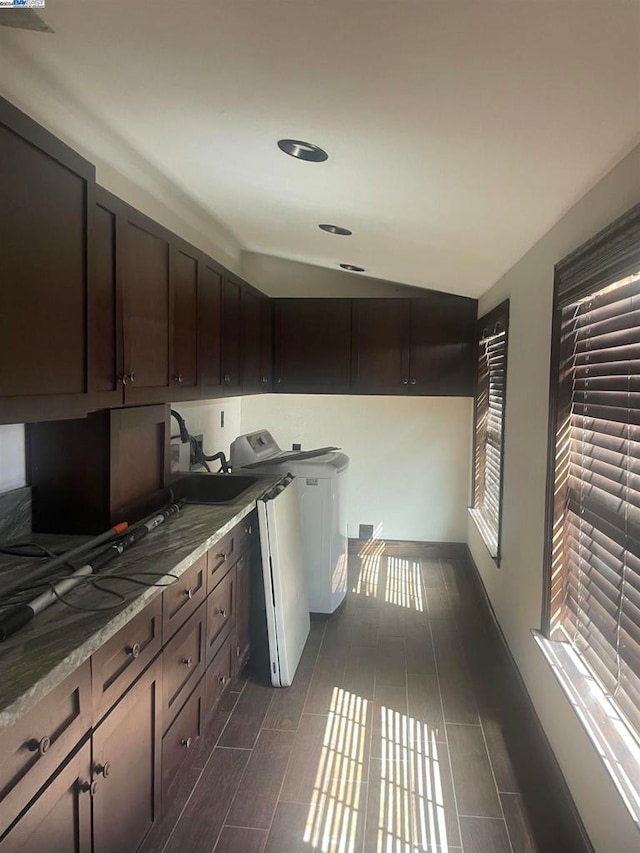 kitchen with vaulted ceiling, light stone countertops, dark brown cabinets, washer / dryer, and sink