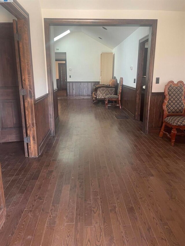 hallway with vaulted ceiling, wood walls, and dark hardwood / wood-style floors