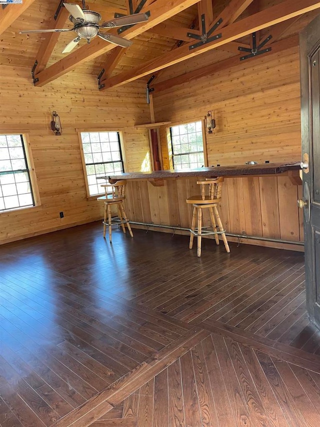 empty room with high vaulted ceiling, wooden walls, beam ceiling, and dark hardwood / wood-style floors