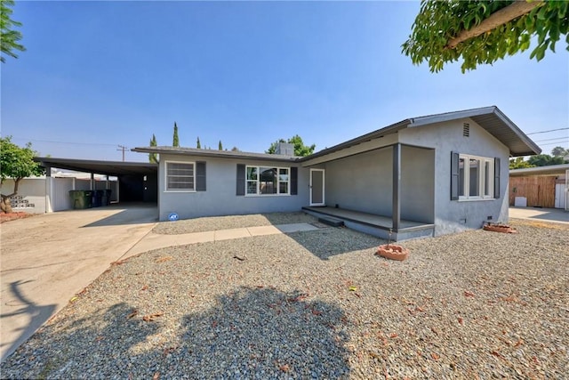 view of front facade with a carport, concrete driveway, fence, and stucco siding