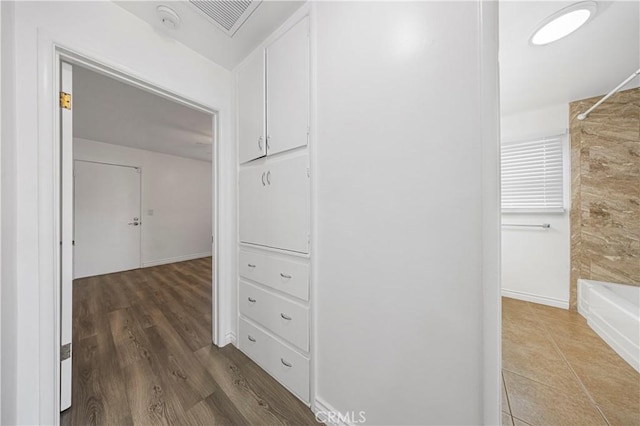 hall with baseboards, wood finished floors, and visible vents