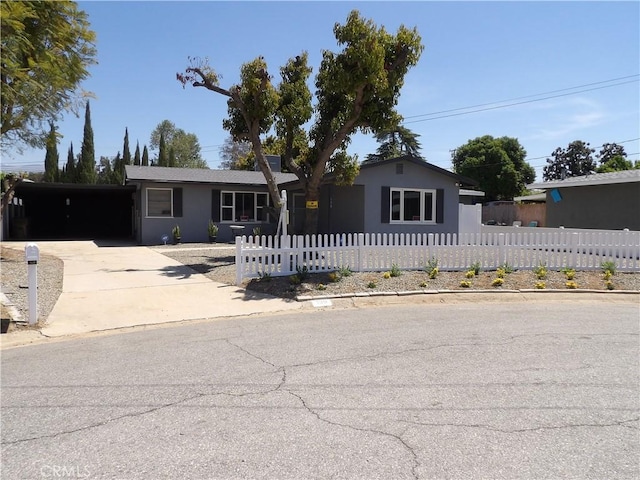 ranch-style house featuring stucco siding, a carport, concrete driveway, and a fenced front yard