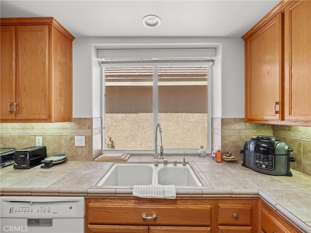 kitchen with white dishwasher, tile countertops, sink, and tasteful backsplash