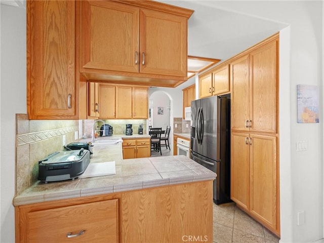 kitchen featuring kitchen peninsula, stainless steel fridge, sink, and decorative backsplash