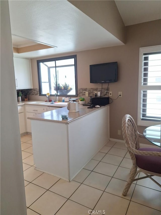 kitchen with white cabinetry, decorative backsplash, kitchen peninsula, and light tile patterned flooring