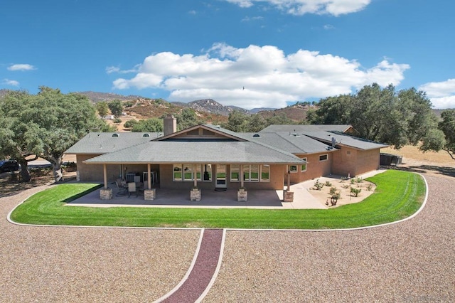 rear view of property with a lawn, a mountain view, and a patio area