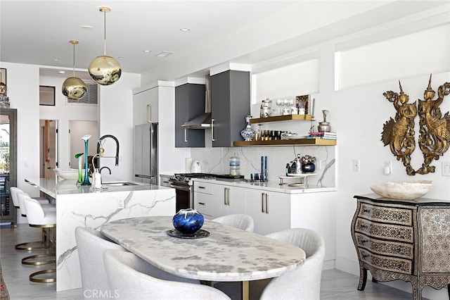 kitchen featuring appliances with stainless steel finishes, white cabinets, decorative light fixtures, and wall chimney range hood