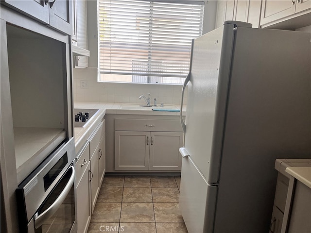 kitchen featuring light tile patterned flooring, oven, white cabinetry, black electric stovetop, and white fridge