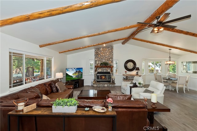 living room with vaulted ceiling with beams, hardwood / wood-style floors, a healthy amount of sunlight, and a stone fireplace