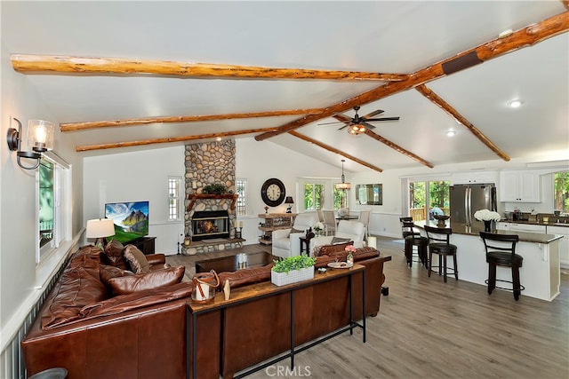 living room featuring a stone fireplace, vaulted ceiling with beams, dark hardwood / wood-style floors, and ceiling fan