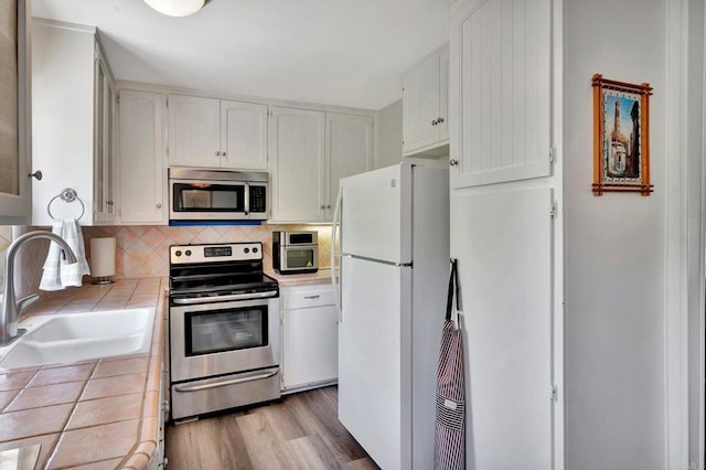 kitchen featuring sink, stainless steel appliances, tasteful backsplash, white cabinets, and tile countertops