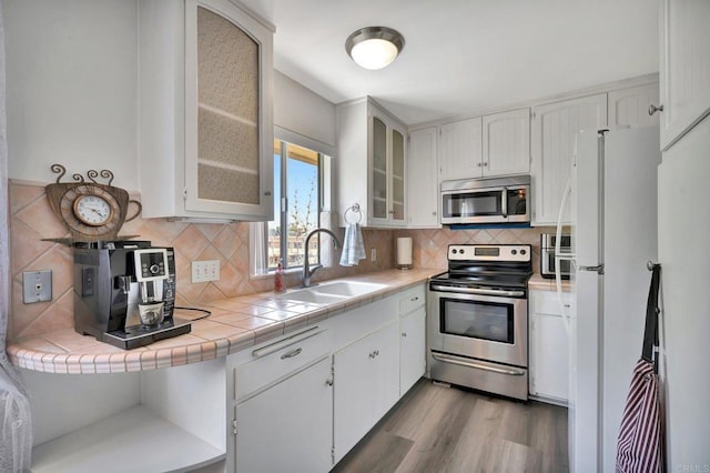 kitchen featuring sink, tile counters, stainless steel appliances, decorative backsplash, and white cabinets