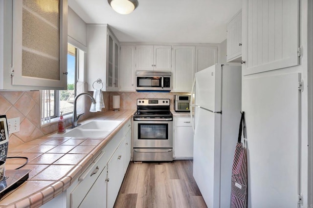 kitchen with tile countertops, white cabinetry, sink, stainless steel appliances, and light wood-type flooring