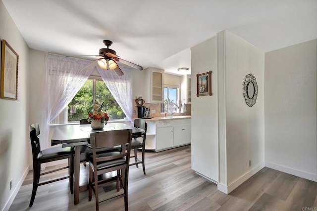 dining space with light wood finished floors, a ceiling fan, and baseboards